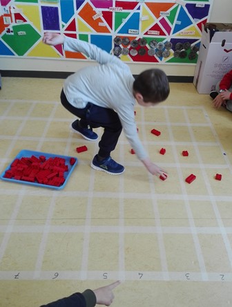 Bambino posiziona mattoncini di lego all'interno di una grande scacchiera disegnata sul pavimento. Bambino posiziona mattoncini di lego all'interno di una grande scacchiera disegnata sul pavimento.